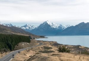 Breathtaking view of Mount Cook with a winding road, lake, and snow-capped peaks in New Zealand.