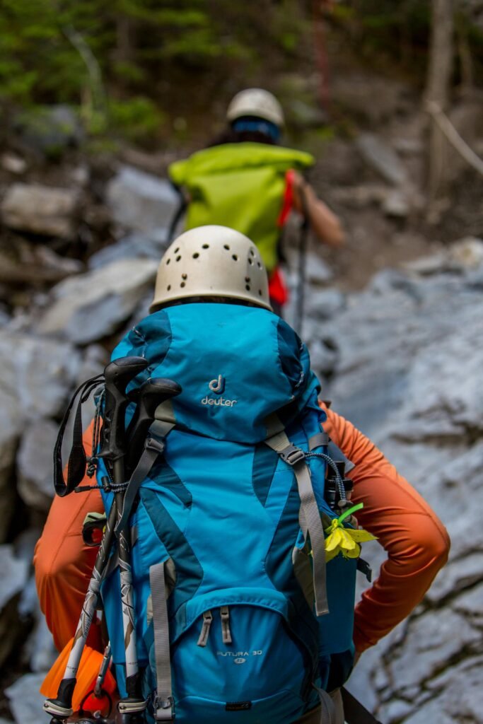 Two hikers with backpacks and helmets navigating a rocky trail in the forest.